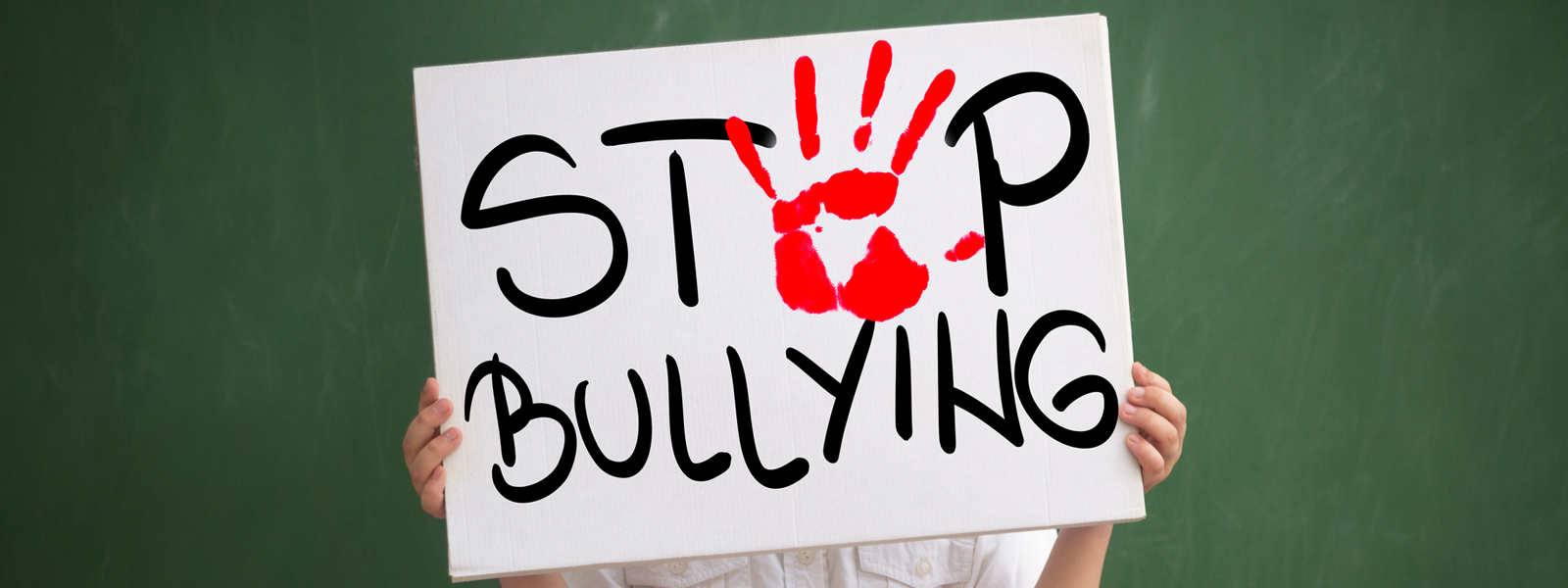 student holding a sign with red palm print and text stop bullying against a green chalkboard background